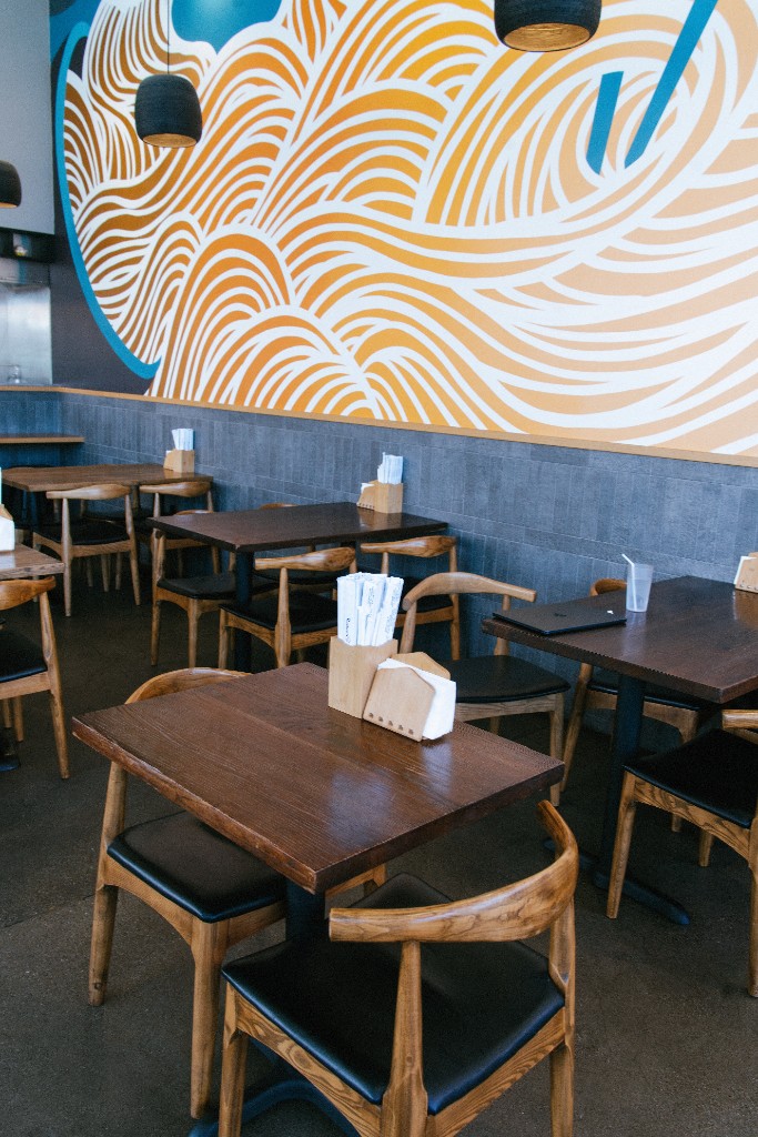 Ramen Hiroshi dining room with wooden tables and a vibrant noodle-inspired wall mural